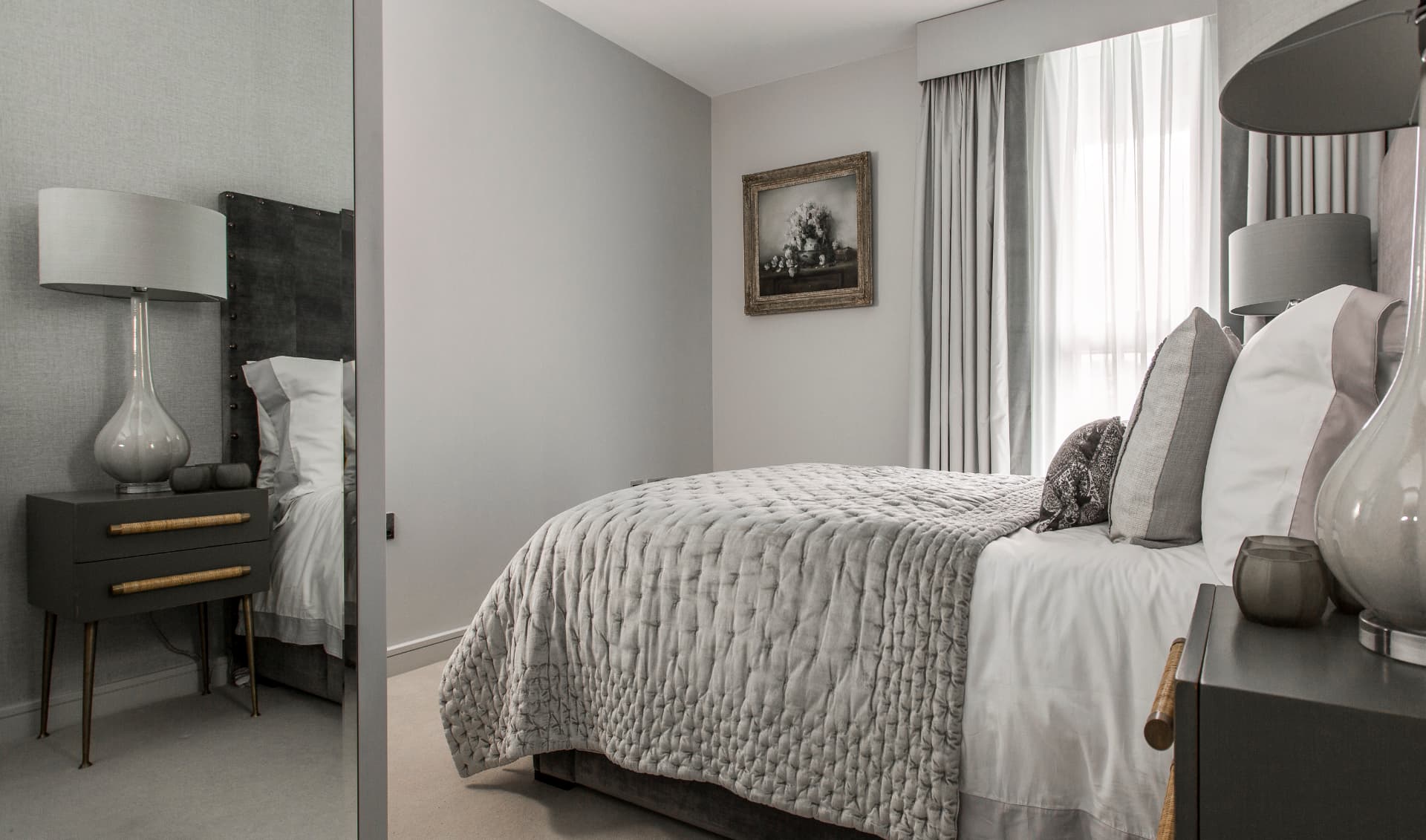 Grey bedroom with a quilted bedspread and glass table lamps.