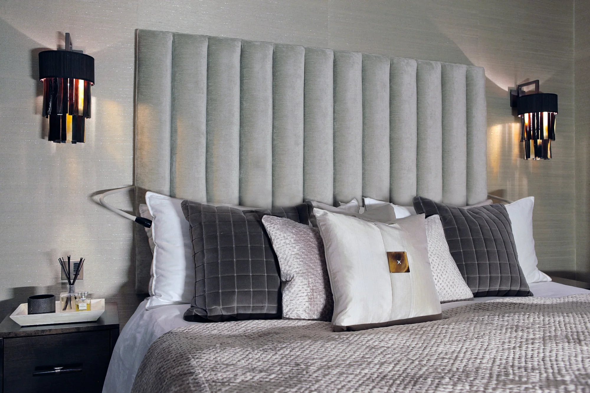 Bedroom with a tailored upholstered headboard and dark wall lights.