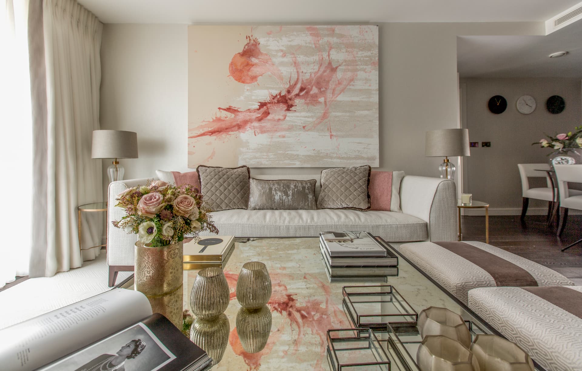 Living room with a mirrored coffee table, blush artwork and a view toward the dining area.