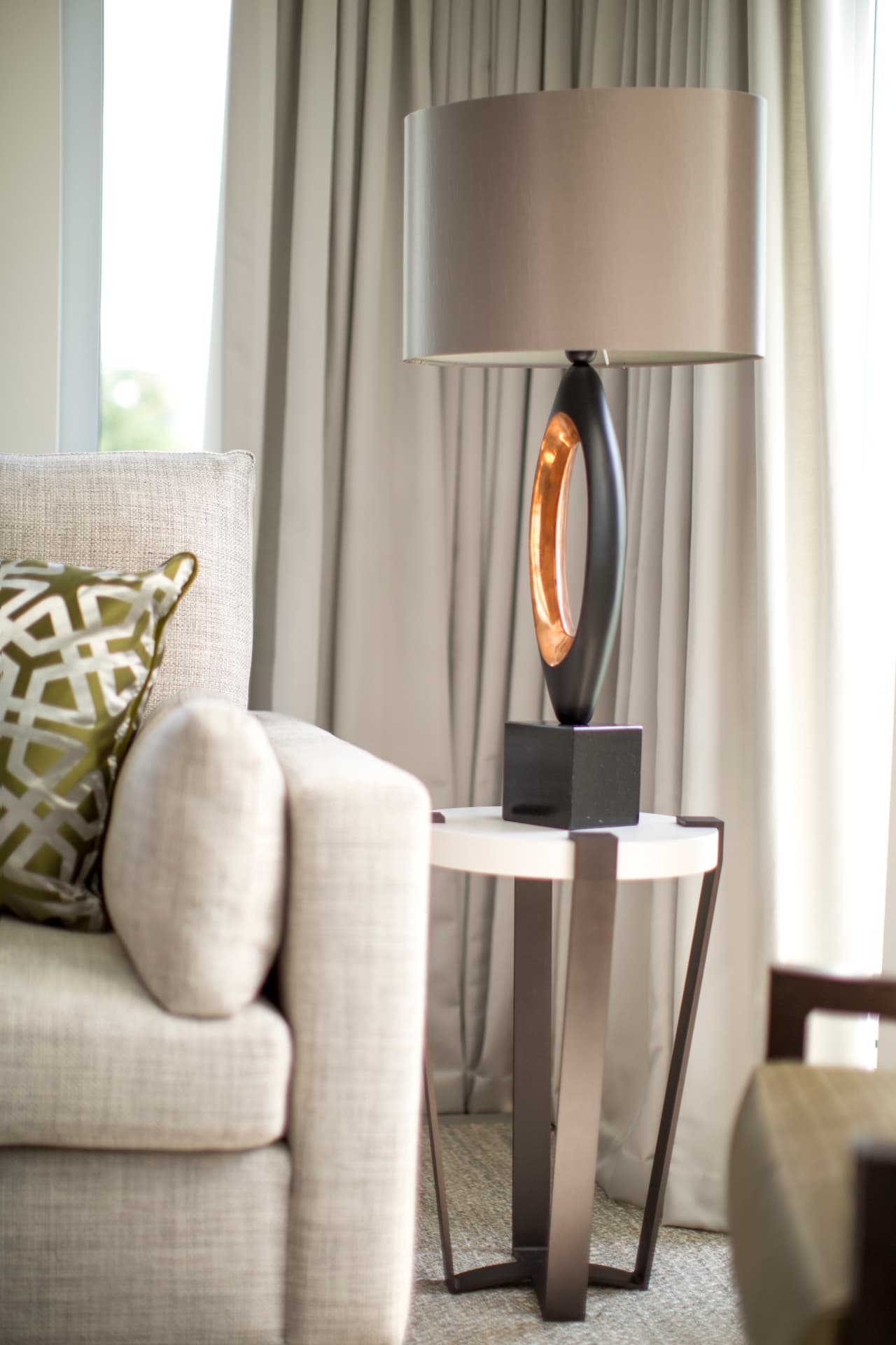 Living room detail with an armchair, sculptural table lamp and round bronze side table at Holland Park.