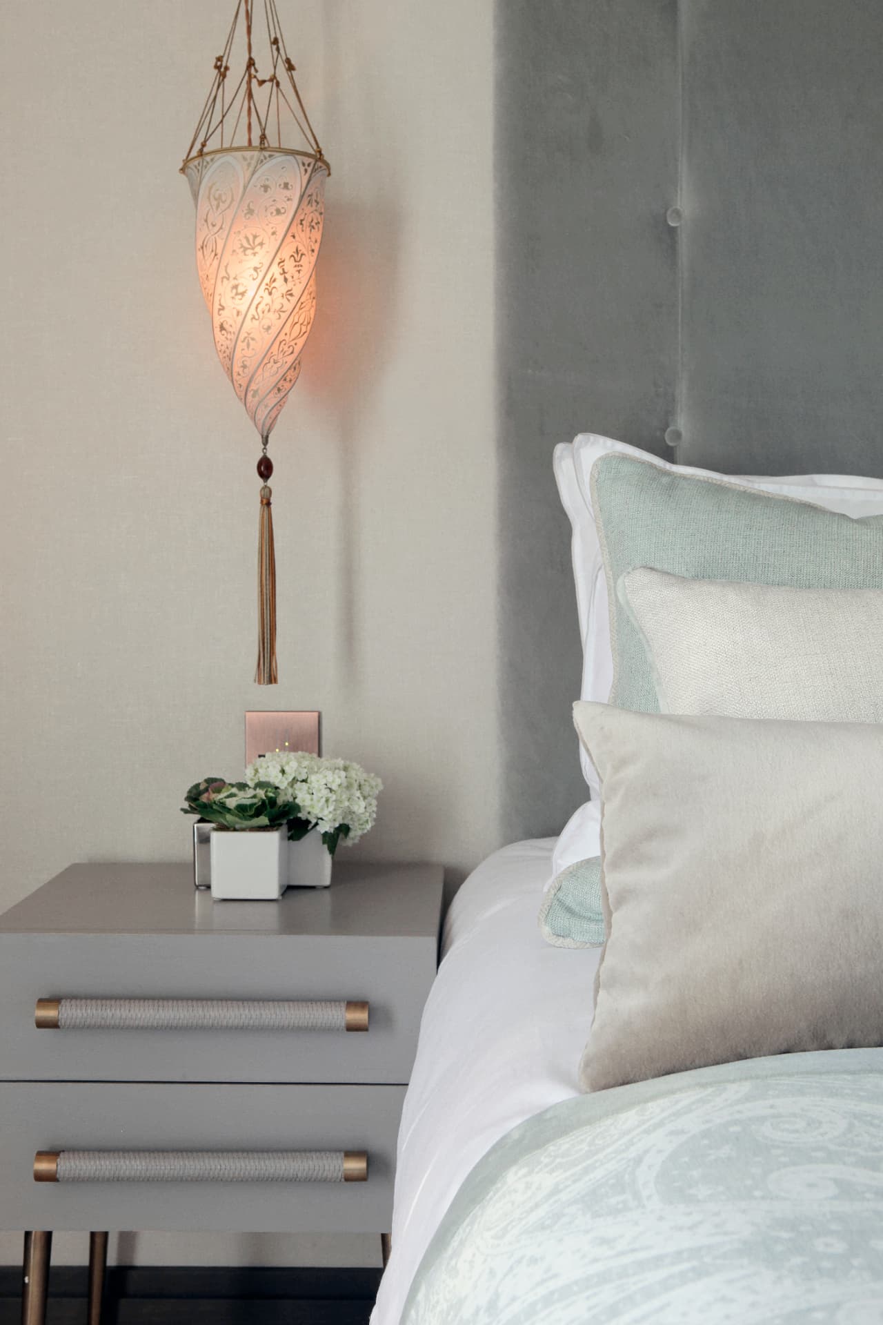 A glowing hanging lantern above a grey bedside table at Kensington Green.
