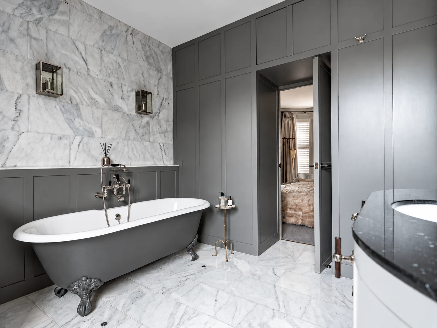 Grey freestanding bath with marble wall and doorway through to the bedroom at Clapham.