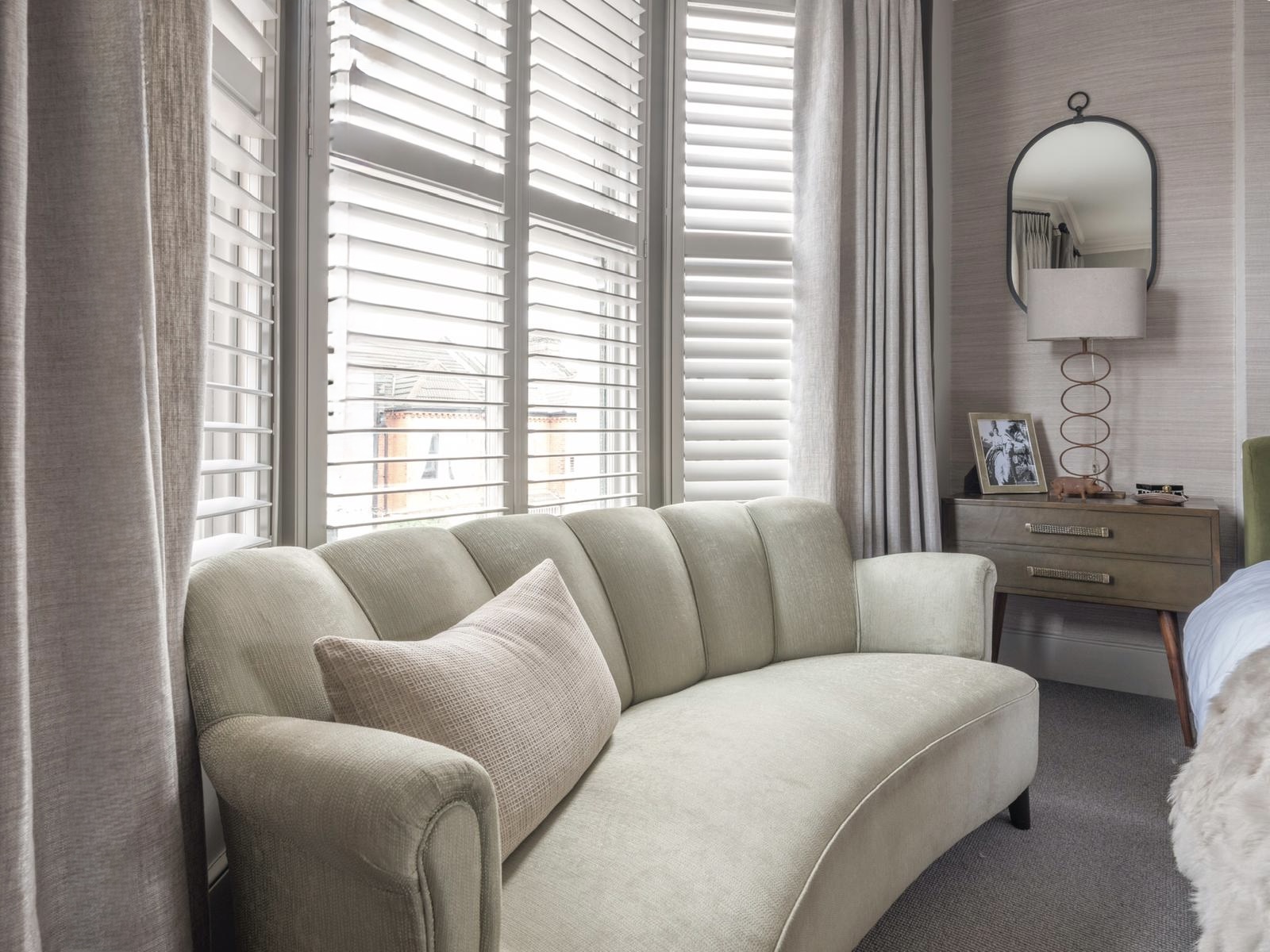 Pale curved sofa beside shuttered windows.