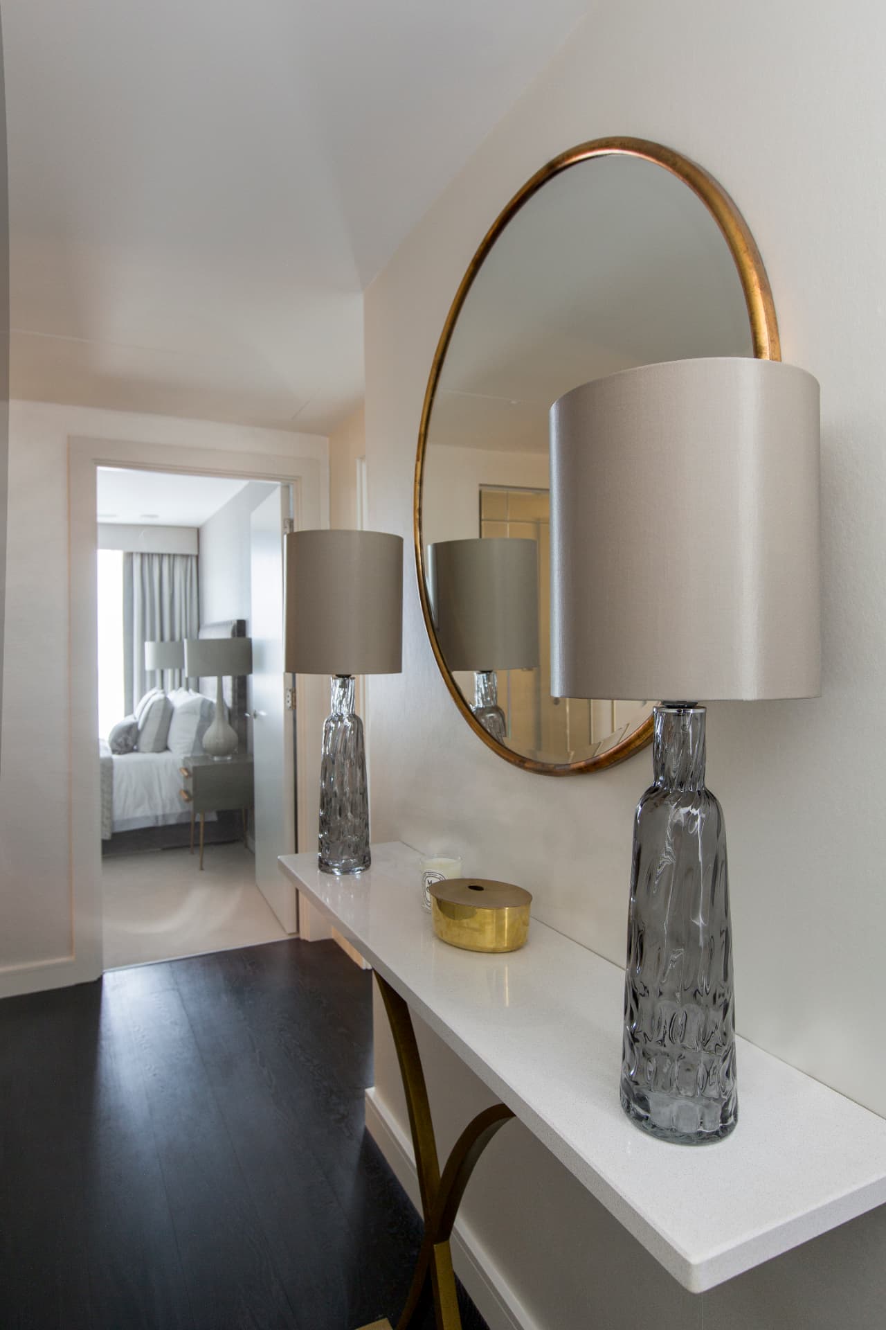 Hallway console with a round brass mirror and glass lamp.