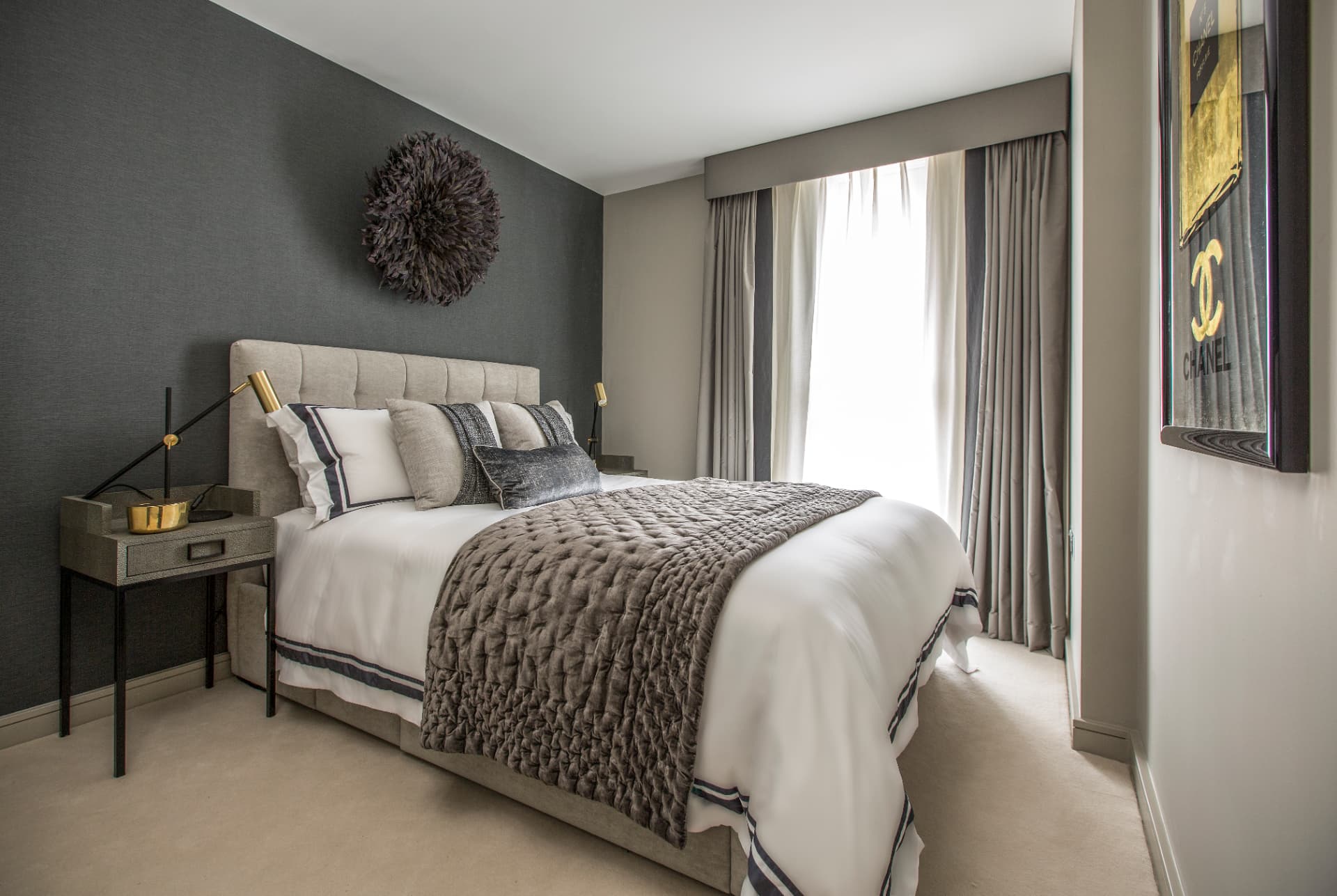 Bedroom with a charcoal wall, feather wall hanging and upholstered headboard.