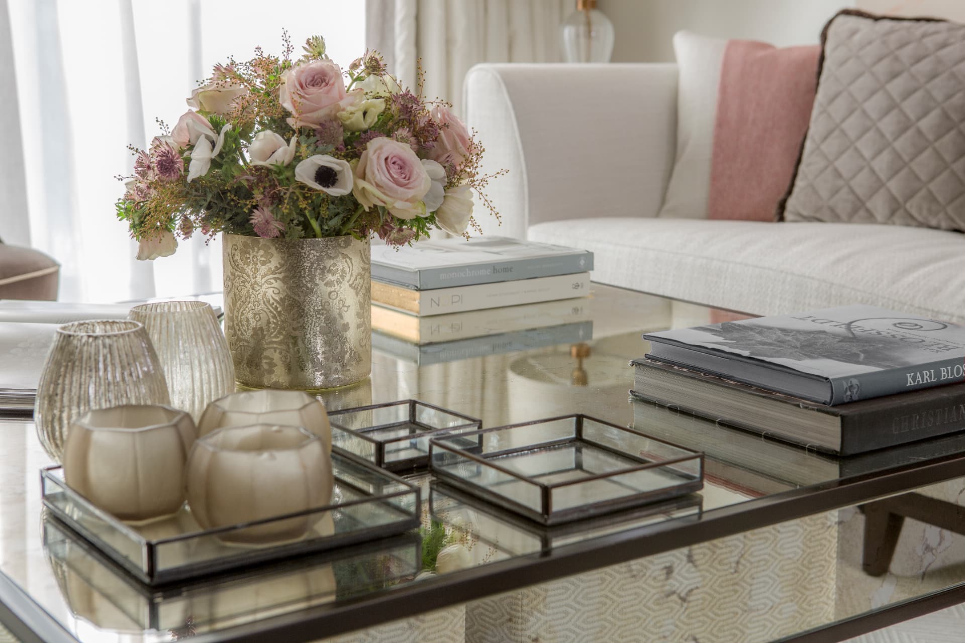 Mirrored coffee table with flowers, books and glass votives in the living room.