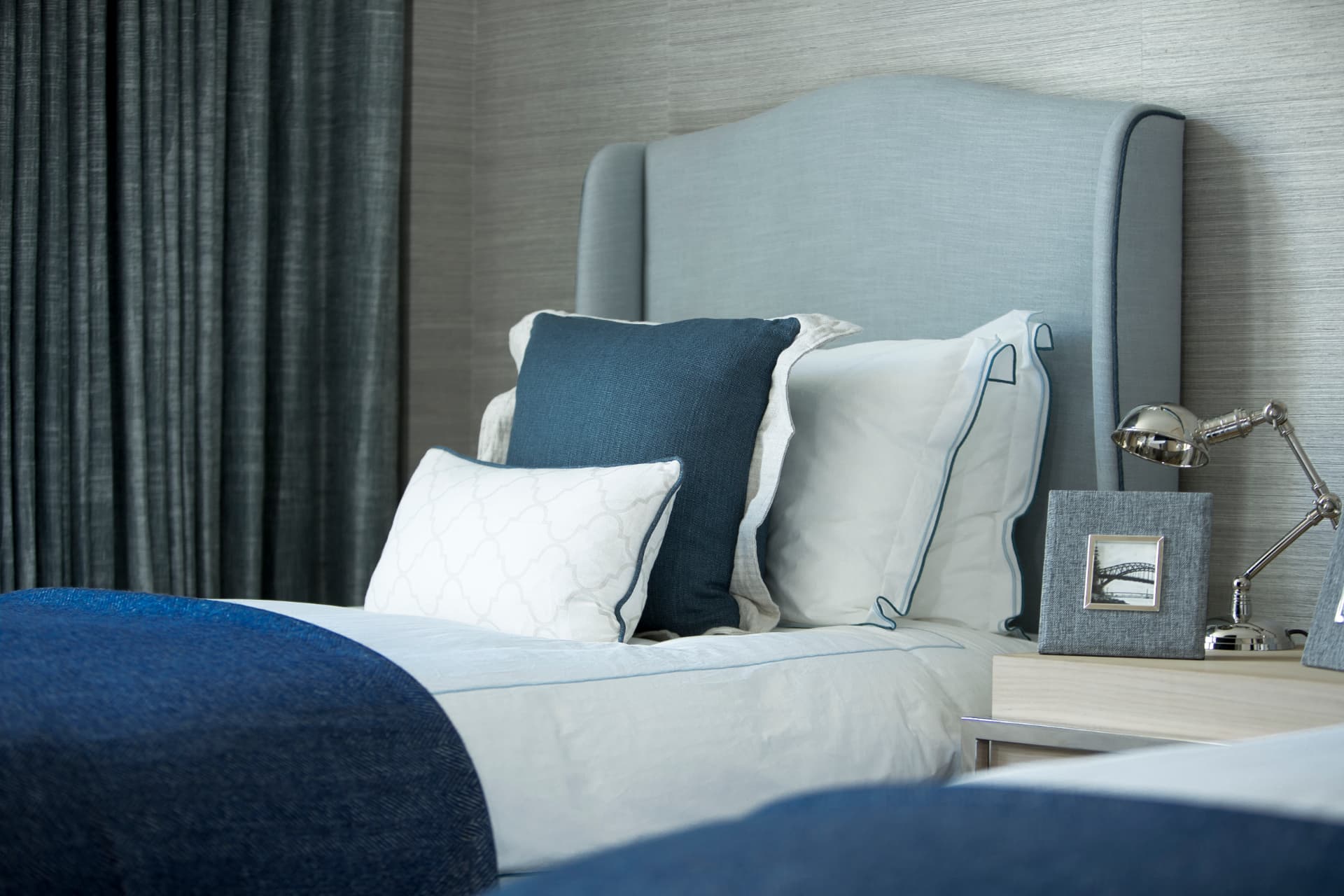 Blue upholstered headboard with navy cushions and a bedside lamp.