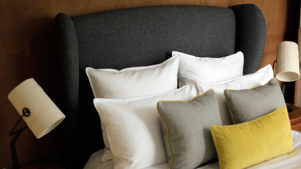 Charcoal headboard dressed with white, grey and yellow cushions.